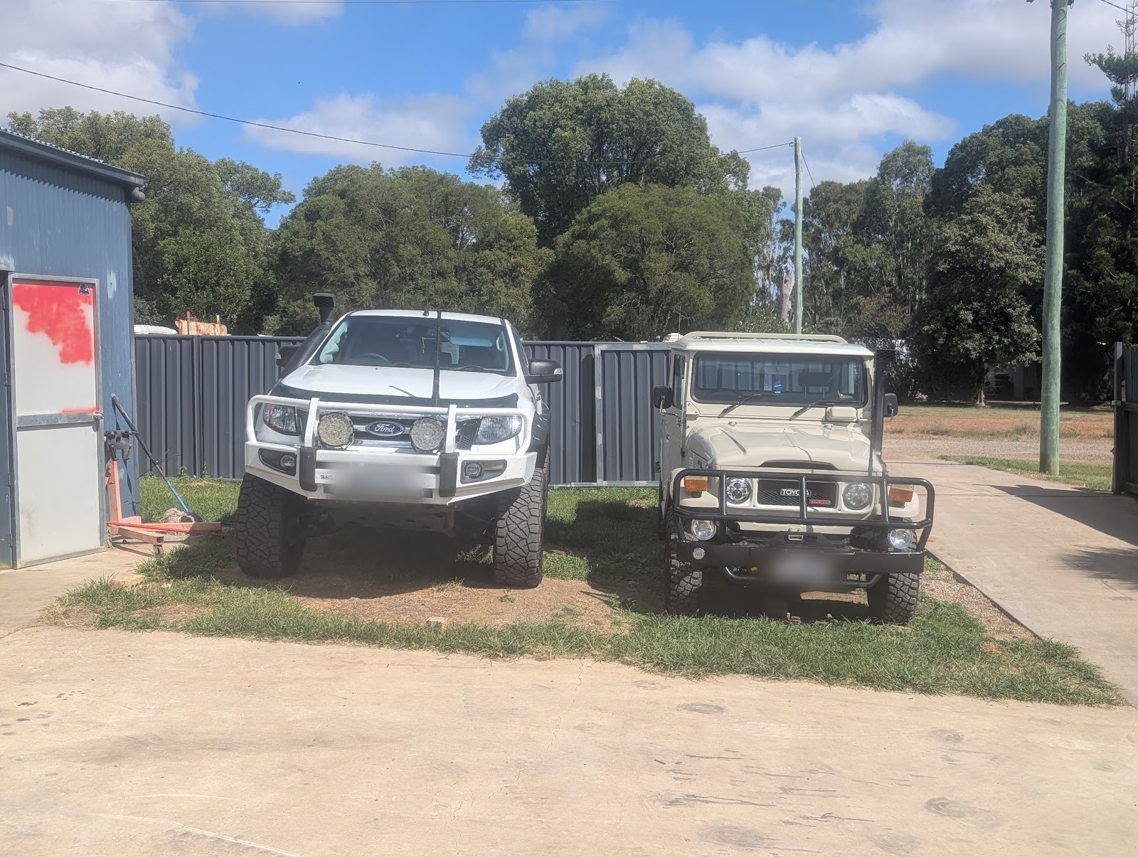 White Ford Ranger and a white FJ40 LandCruiser parked side by side outside the shed